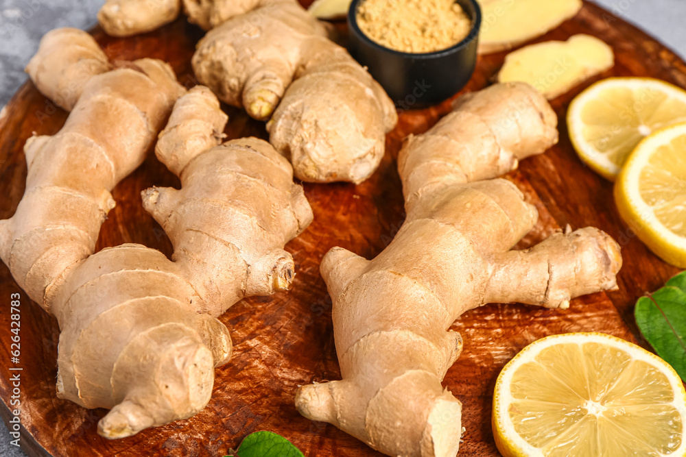 Wooden board with fresh ginger roots, sliced lemon and bowl of dried powder, closeup