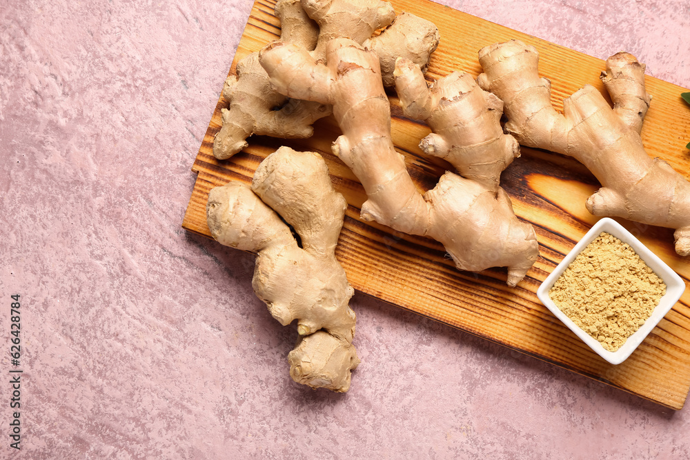 Wooden board with fresh ginger roots and bowl with dried powder on pink background