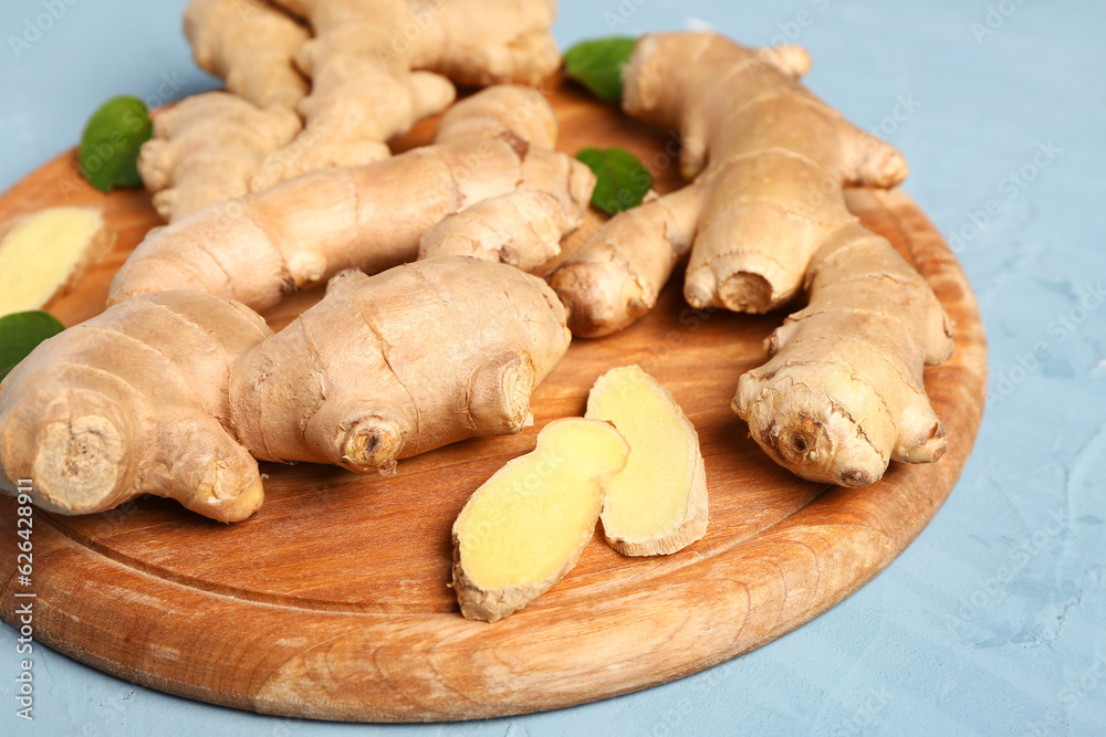 Wooden board with fresh ginger roots and leaves on blue background