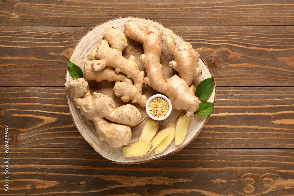 Board with fresh ginger roots and bowl of dried powder on wooden background