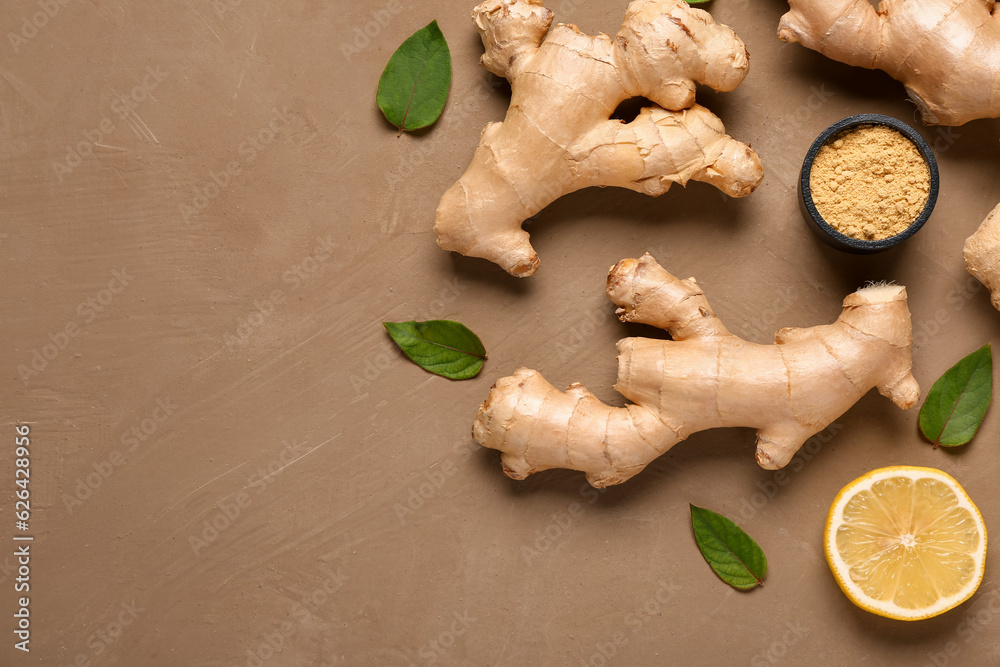 Fresh ginger roots with sliced lemon, leaves and bowl of dried powder on brown background