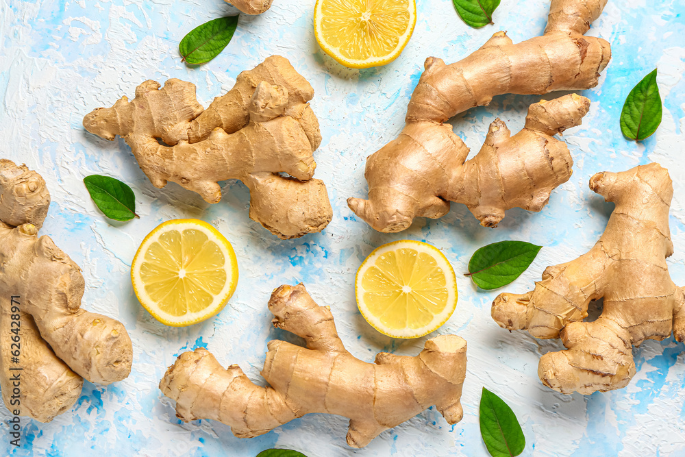 Fresh ginger roots with slices of lemon and leaves on light blue background