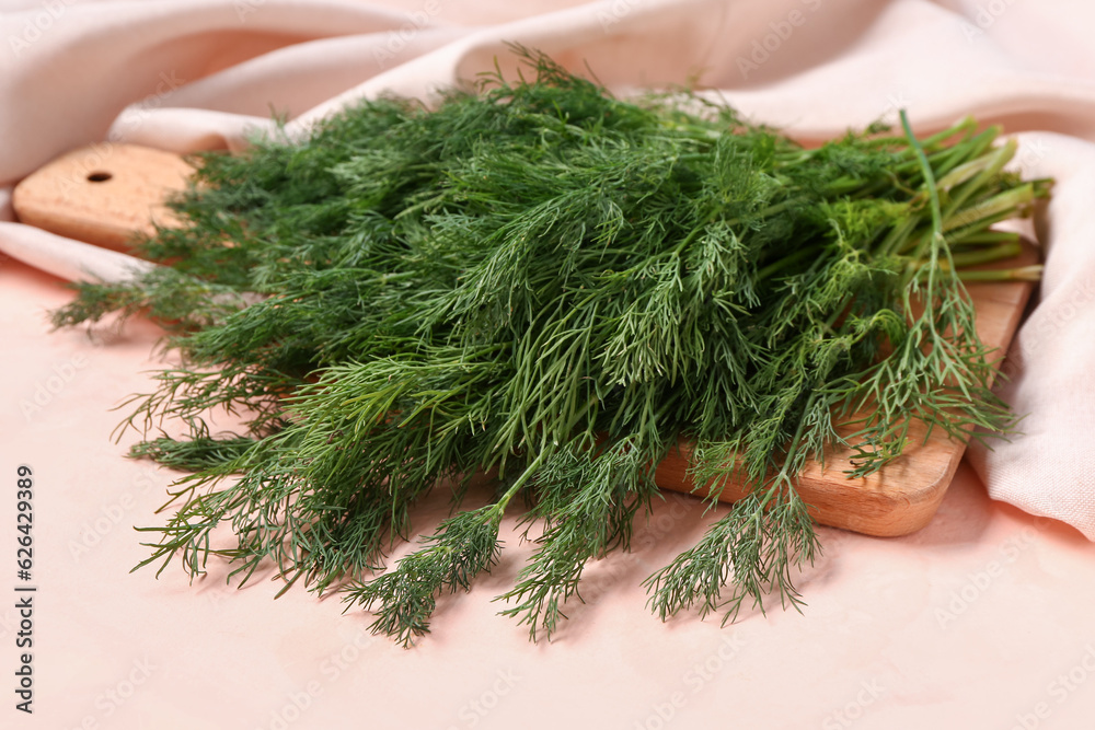 Wooden board with fresh dill on pink background