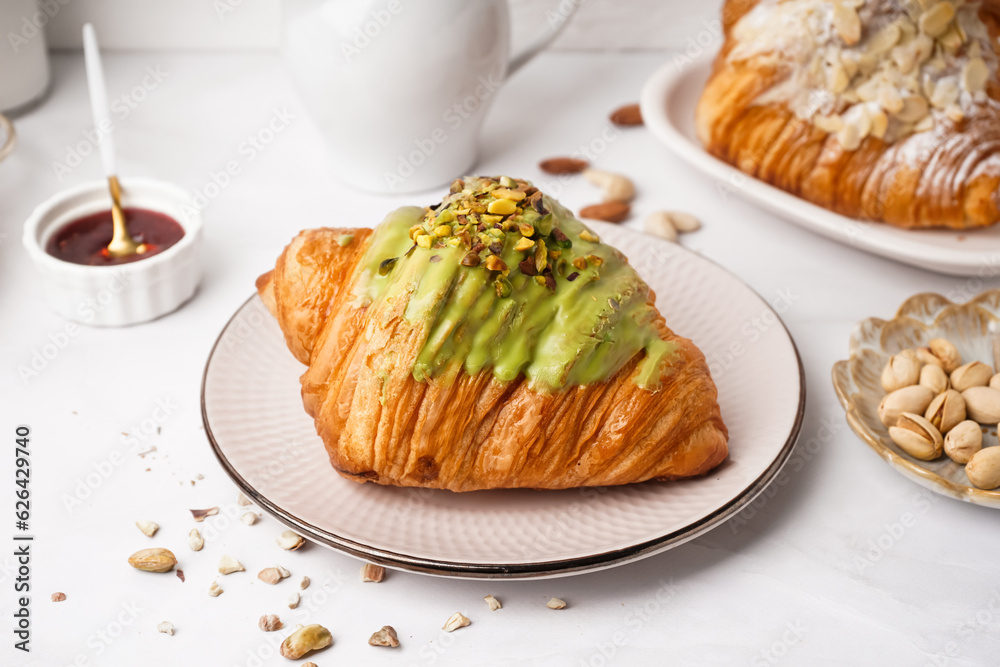 Plate with tasty croissant, pistachio nuts and jam on light table