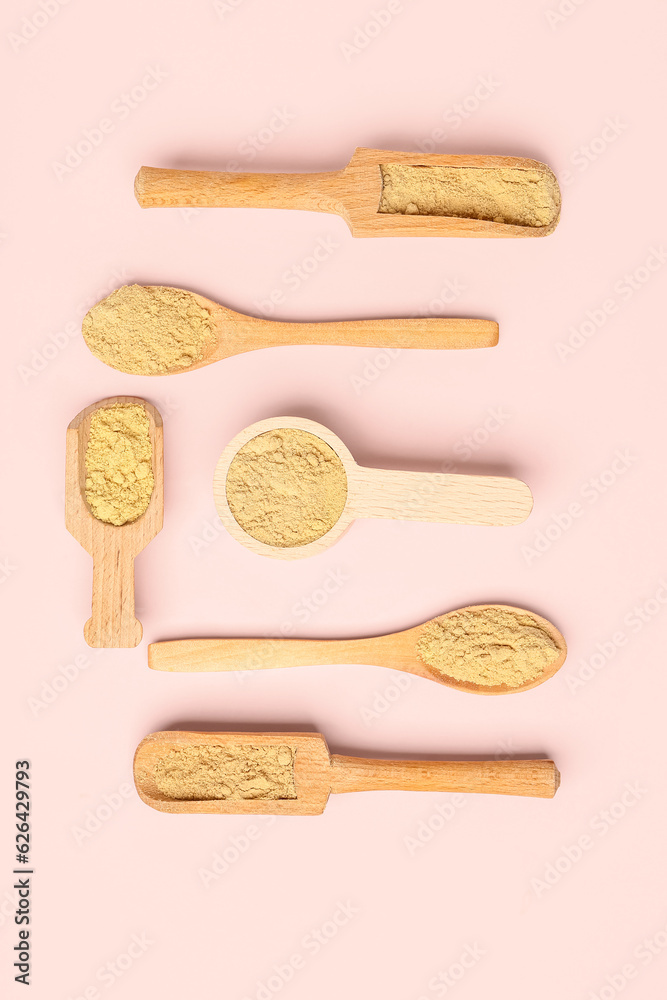 Wooden scoops and spoons with ginger powder on pink background