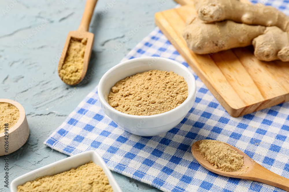 Bowls and wooden spoons with ginger powder on blue background