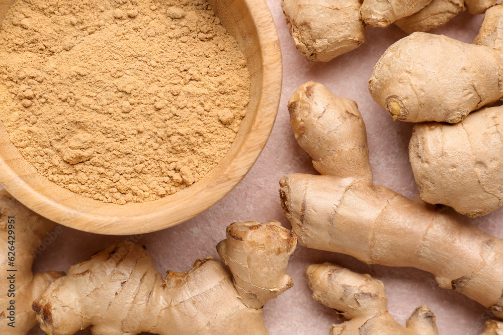 Fresh ginger roots and wooden bowl with dried powder on pink background