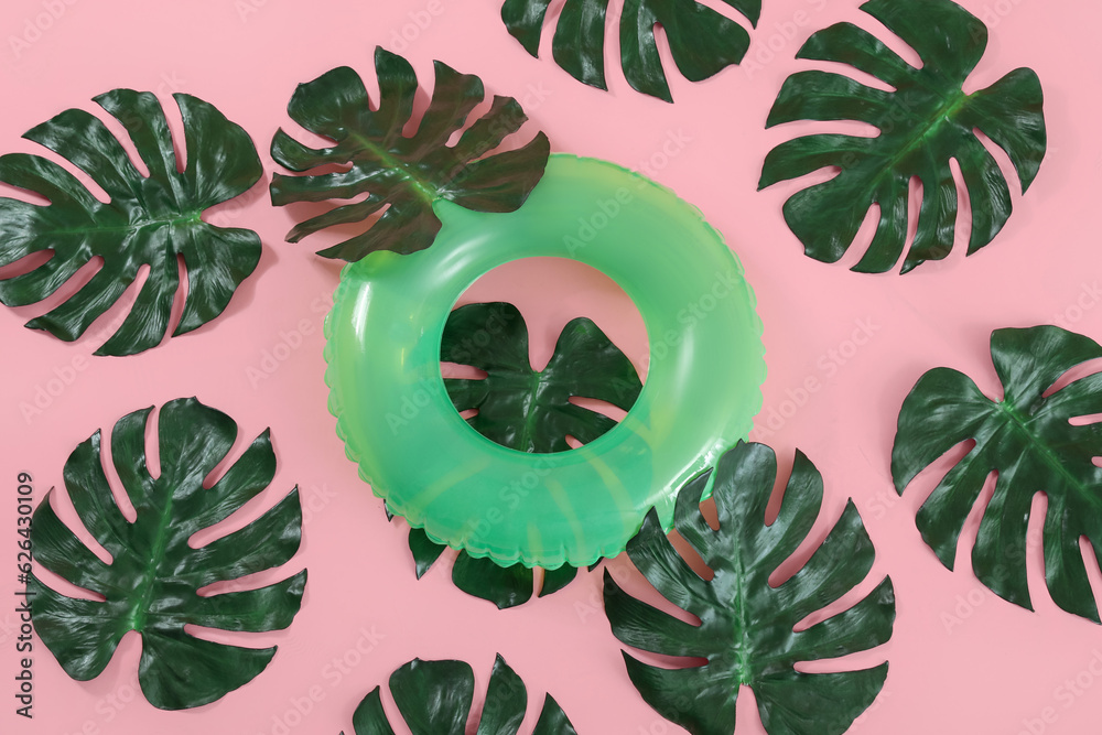 Swim ring with palm leaves on pink background, top view