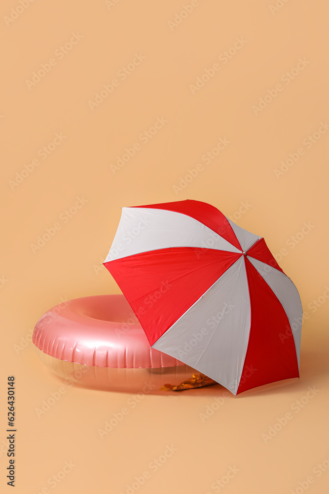 Swim ring with beach umbrella on beige background