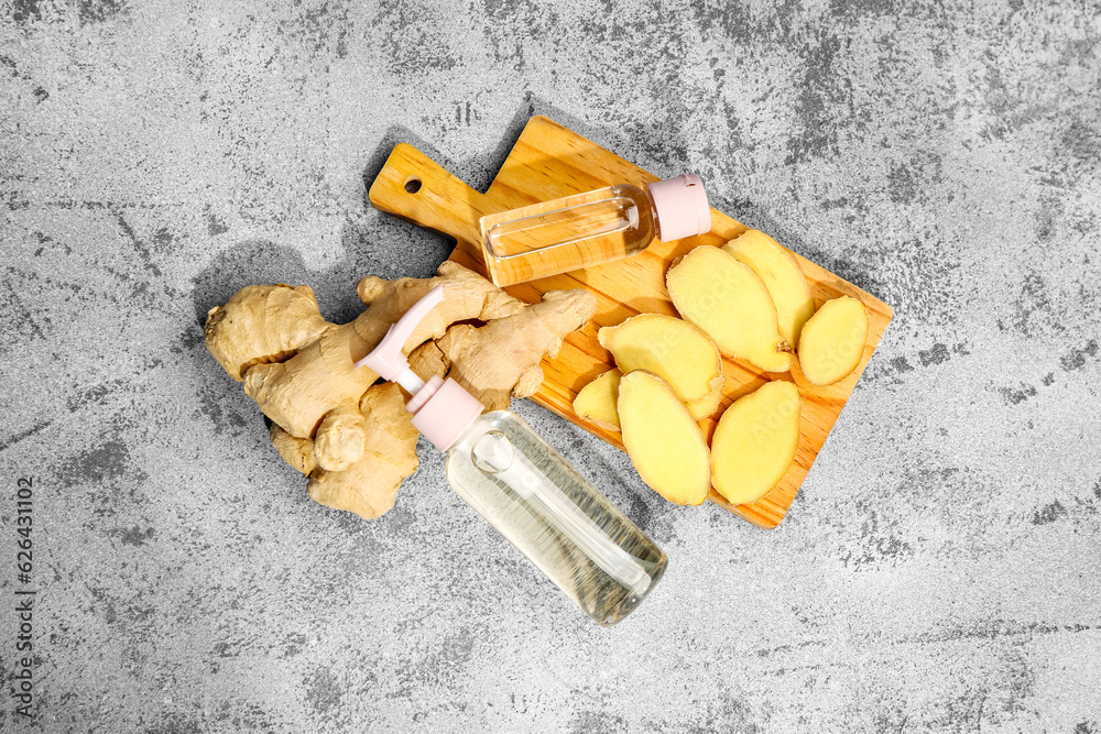 Bottles of cosmetic oil and wooden board with sliced ginger root on grey table