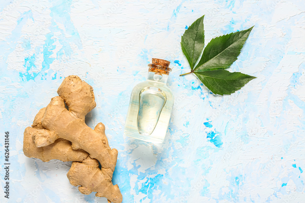 Bottle of ginger cosmetic oil and leaves on light blue background