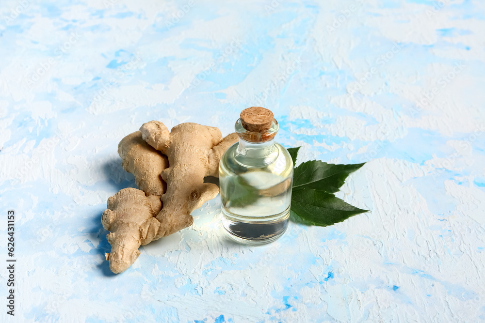 Bottle of ginger cosmetic oil and leaves on light blue background