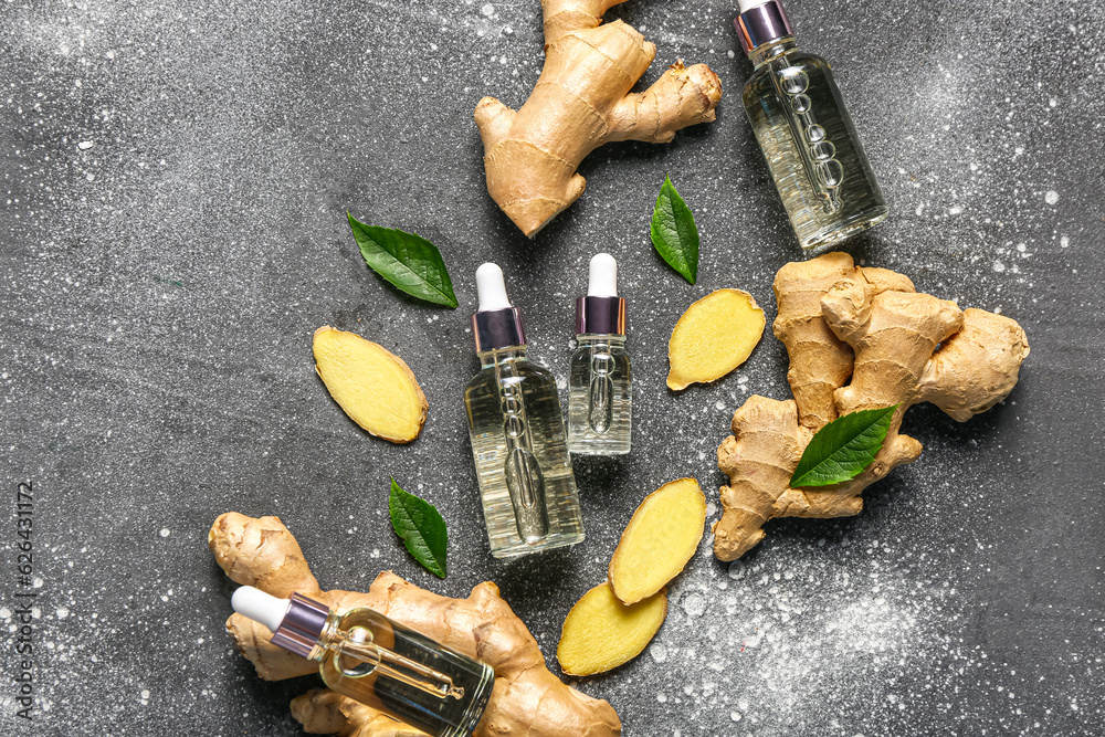 Bottles of ginger cosmetic oil and leaves on grey table