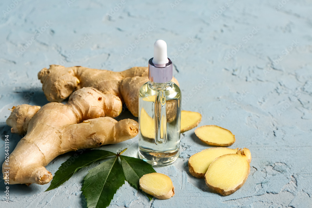 Bottle of ginger cosmetic oil and leaves on blue background