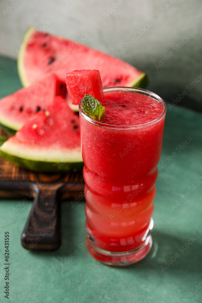 Glass of tasty watermelon juice with mint on green table