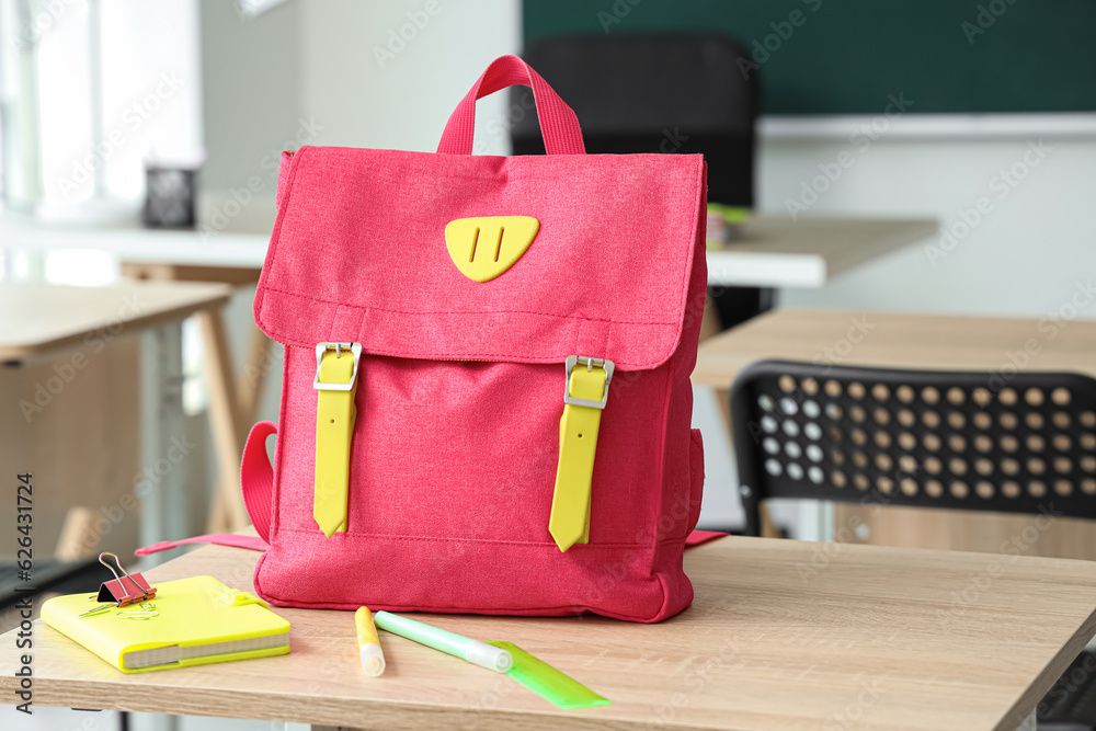 Pink school backpack with stationery on desk in classroom