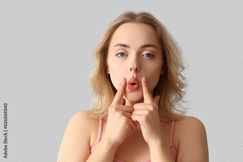 Young woman doing face building exercise on light background, closeup