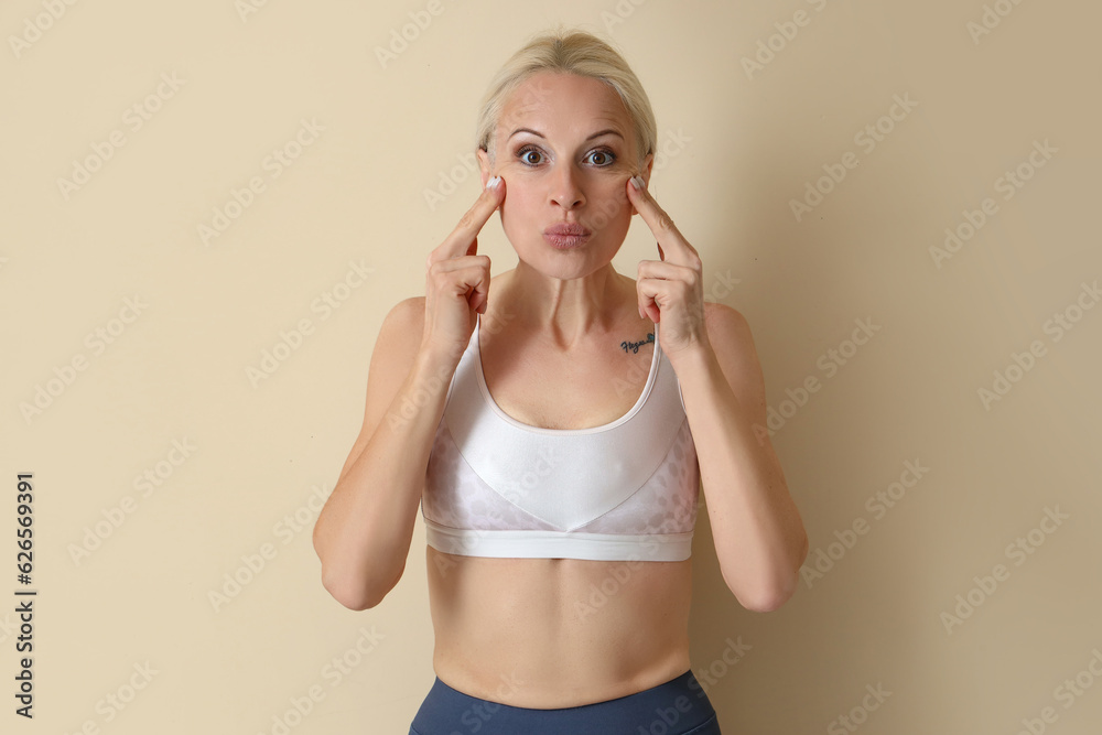 Sporty mature woman doing face building exercise on beige background