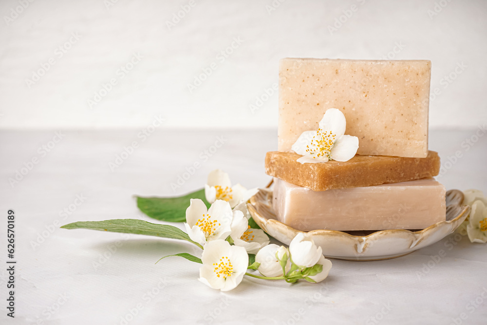 Stack of soap bars and beautiful jasmine flowers on light background