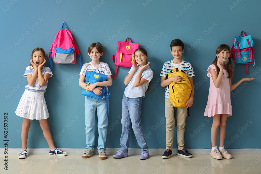 Little pupils with backpacks near blue wall