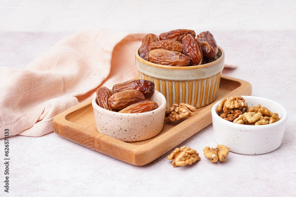 Bowls with dried dates and nuts on light background