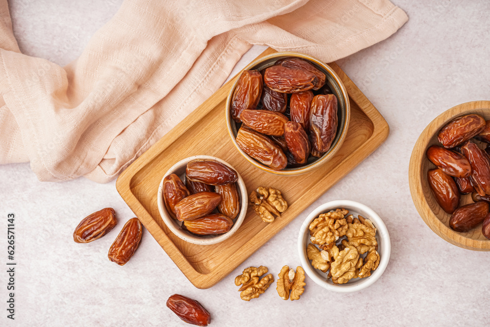 Bowls with dried dates and nuts on light background