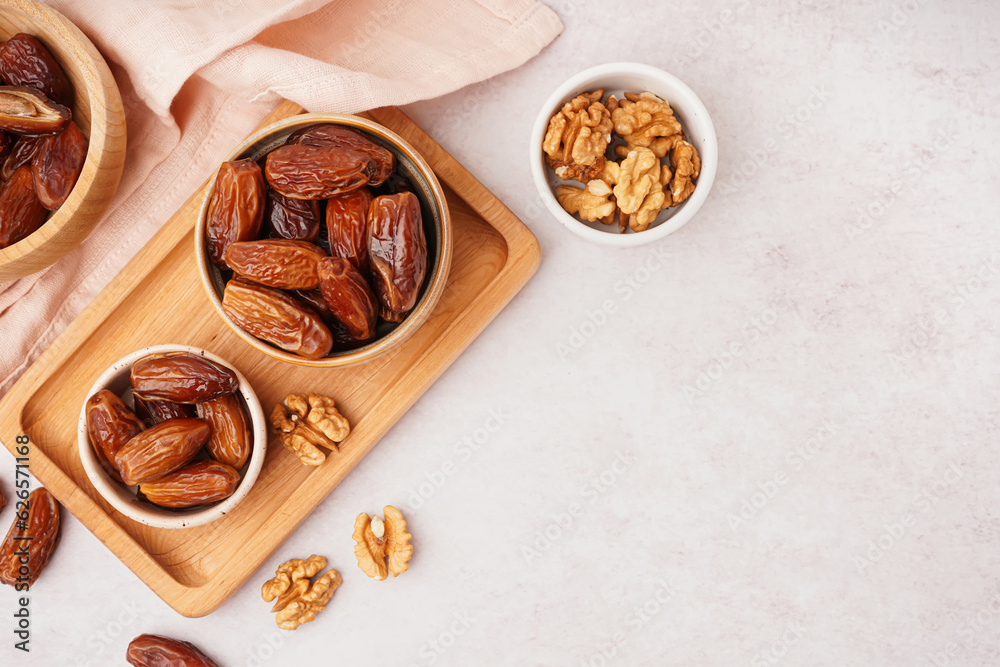 Bowls with dried dates and nuts on light background