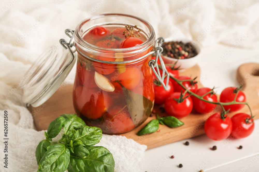 Jar with canned tomatoes and basil on white wooden table