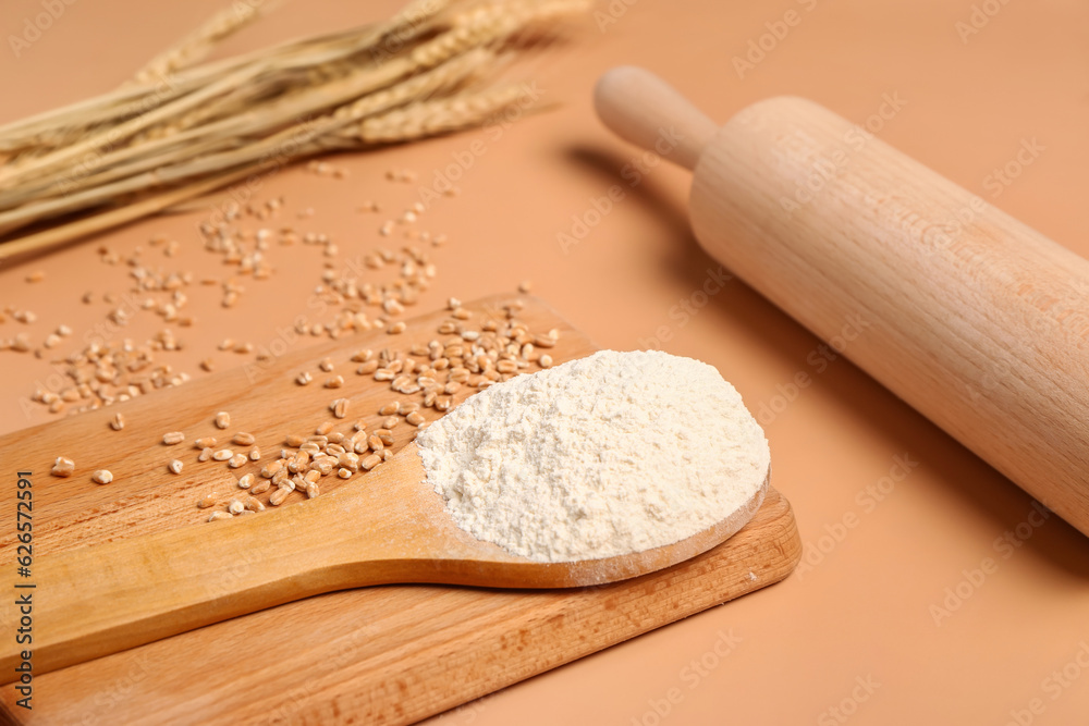 Spoon with flour and wheat grains on beige background, closeup