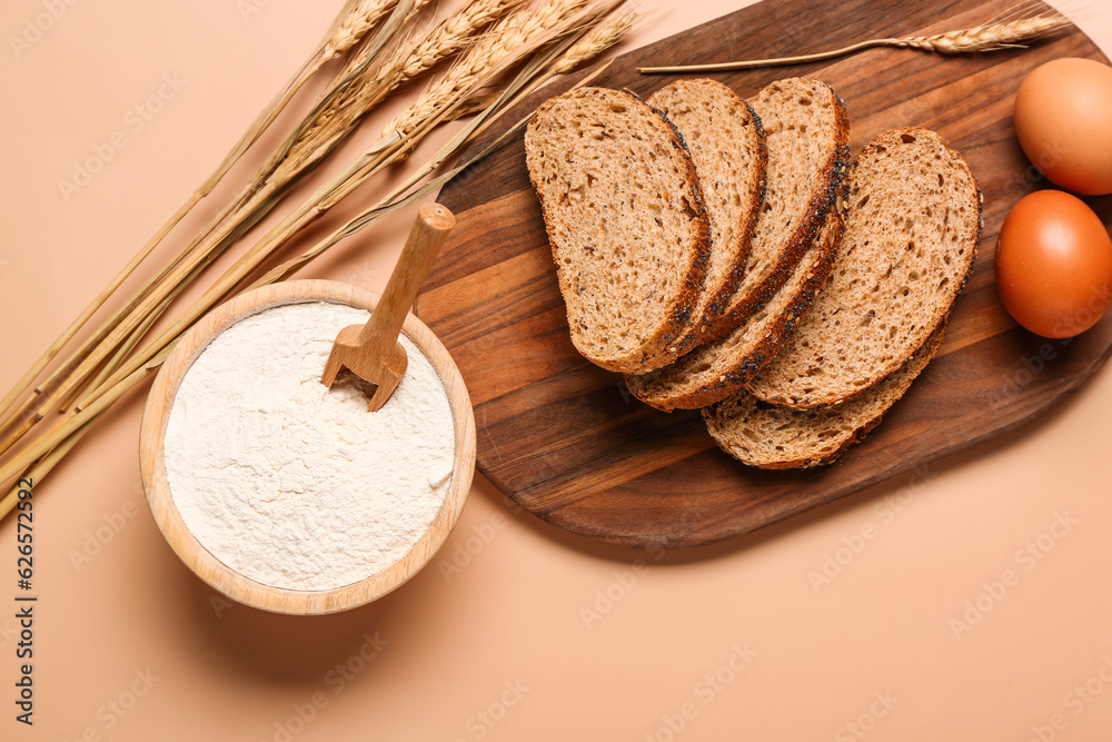 Bowl with flour, bread pieces and wheat ears on beige background