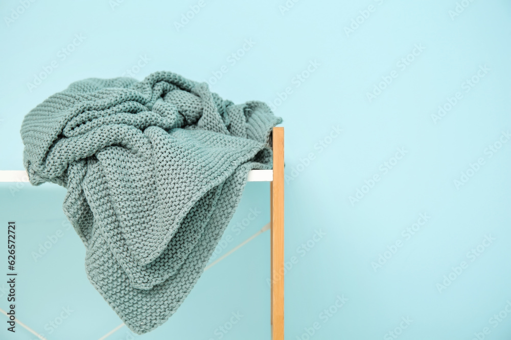 Shelving unit with cozy blanket near blue wall, closeup