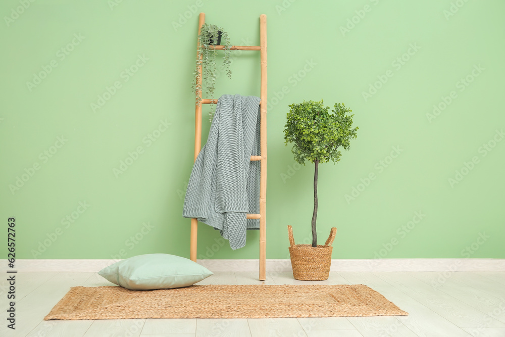 Ladder with cozy blanket near green wall