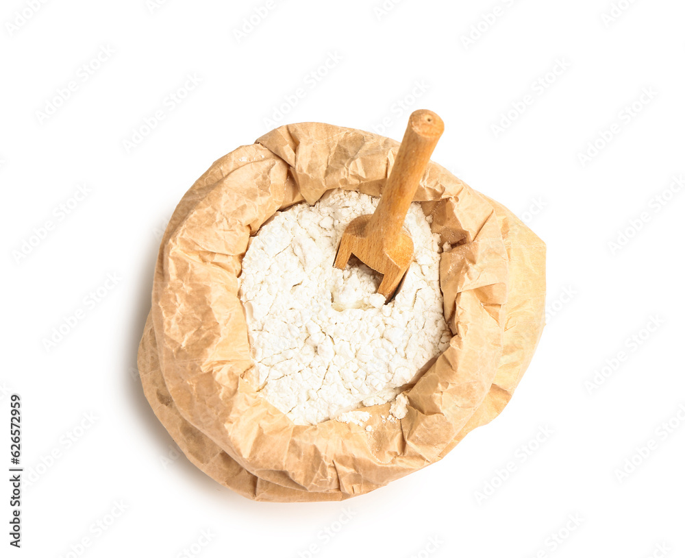 Paper bag with wheat flour and wooden scoop on white background