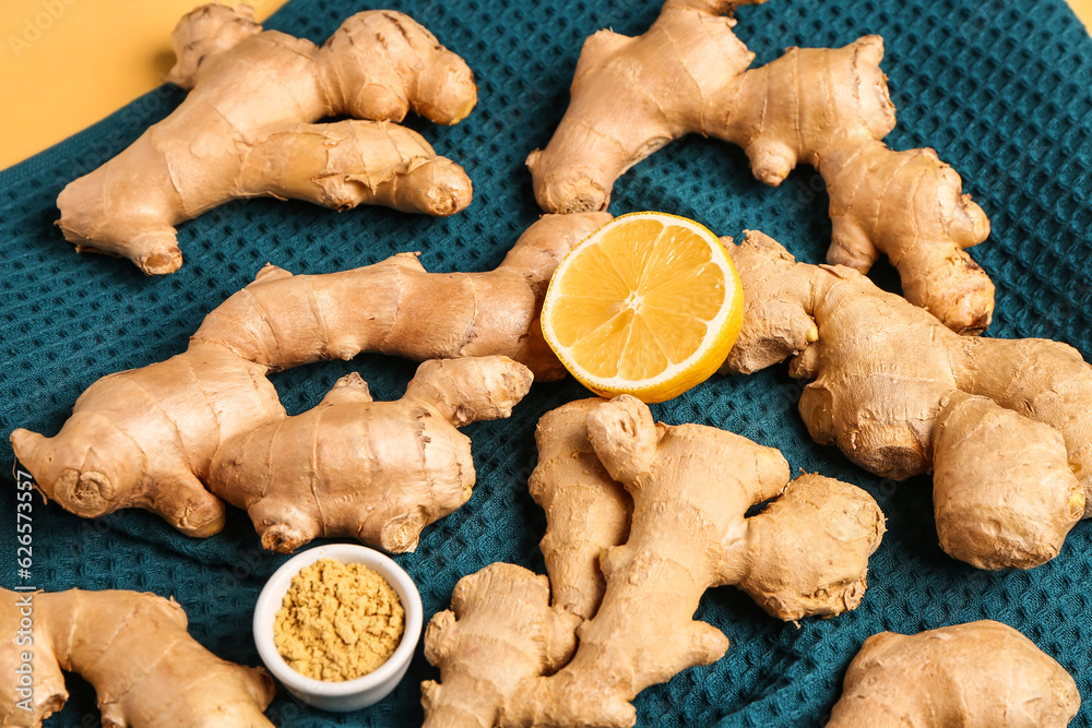 Fresh ginger roots, half of lemon and bowl with dried powder on yellow background, closeup