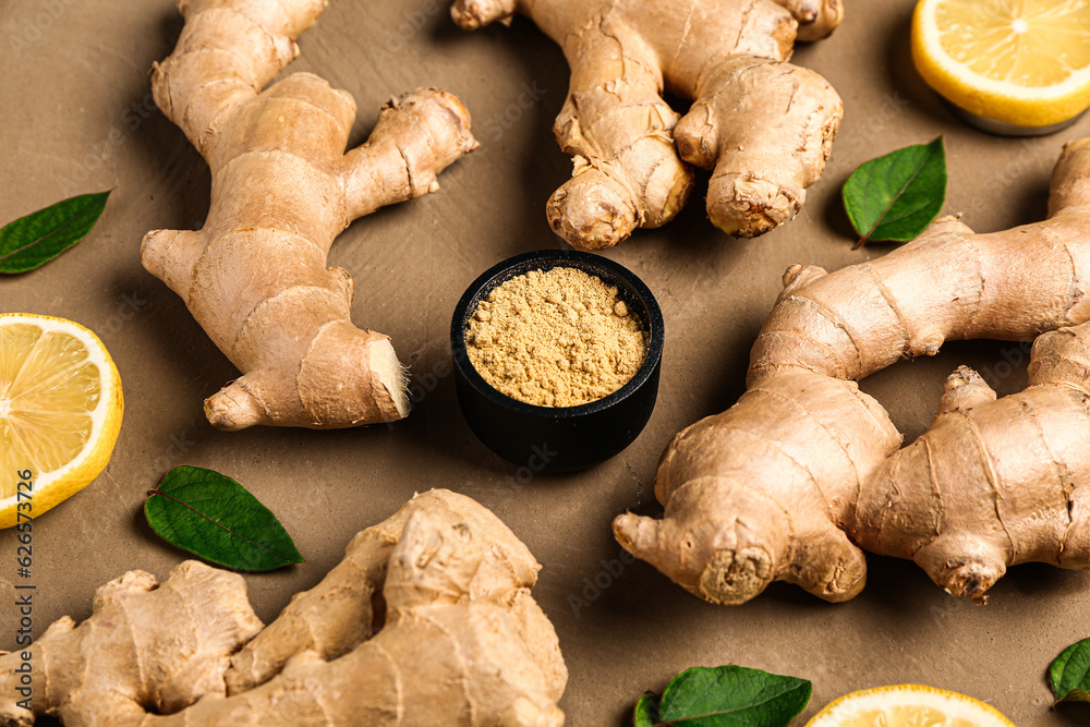 Fresh ginger roots with sliced lemon, leaves and bowl of dried powder on brown background