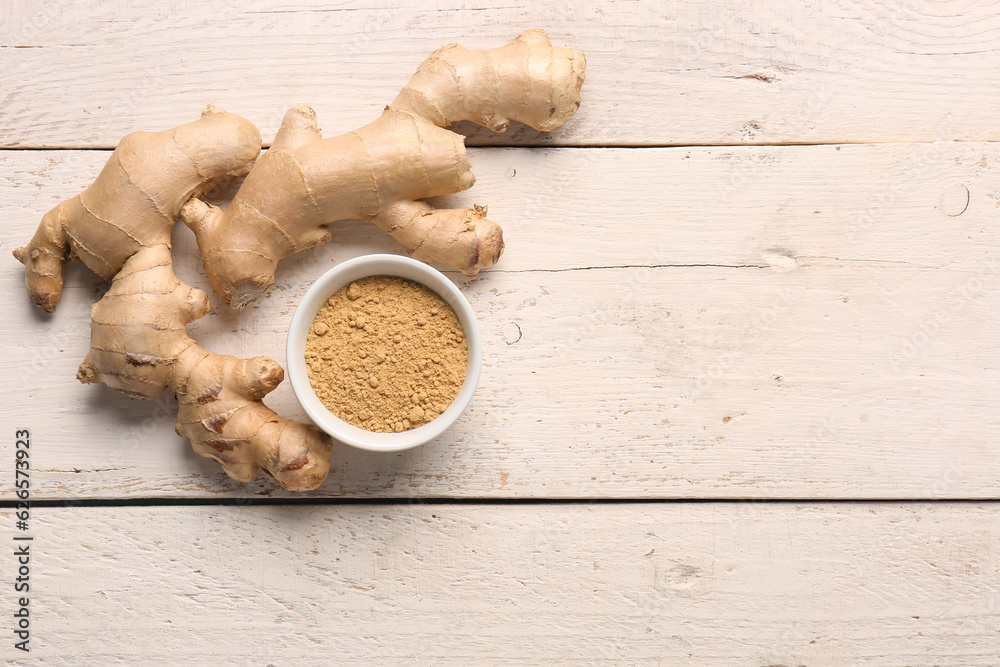 Fresh ginger root and bowl with dried powder on white wooden background