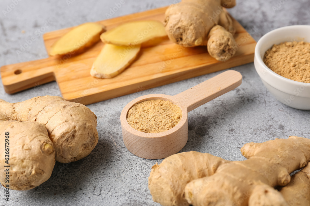 Fresh ginger roots, bowl and wooden spoon with dried powder on blue background