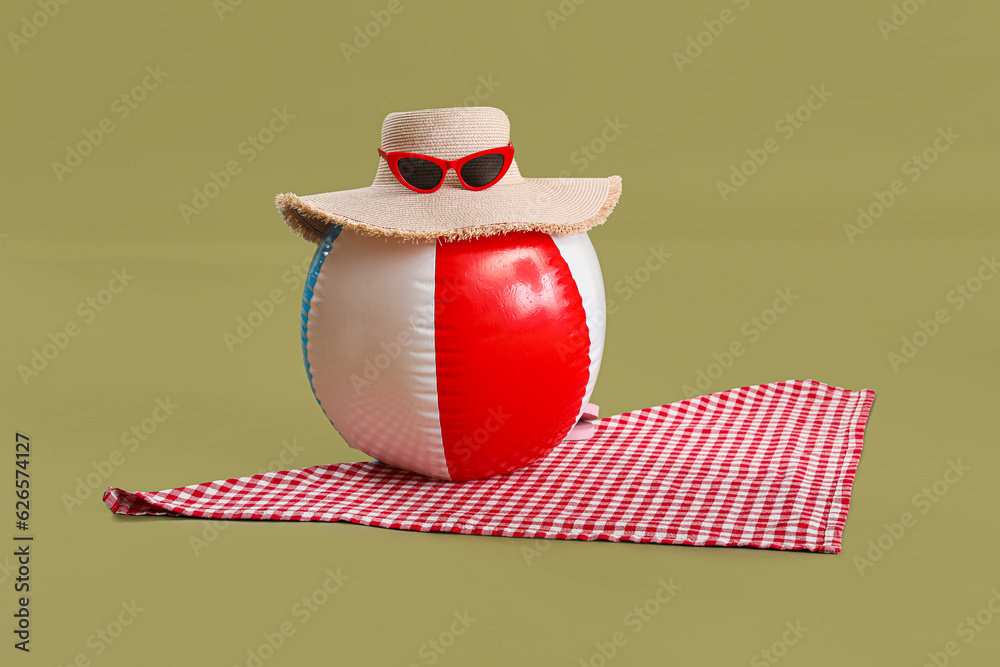 Beach ball with hat, sunglasses and towel on green background