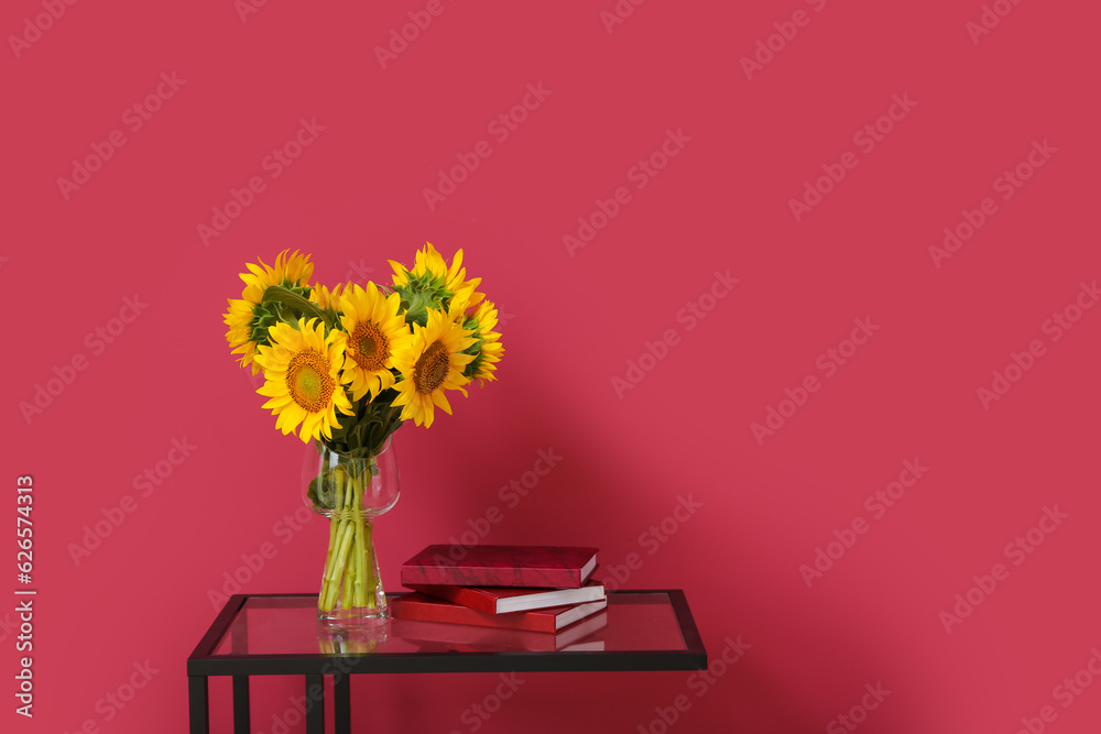 Vase with beautiful sunflowers and books on table near burgundy wall in room