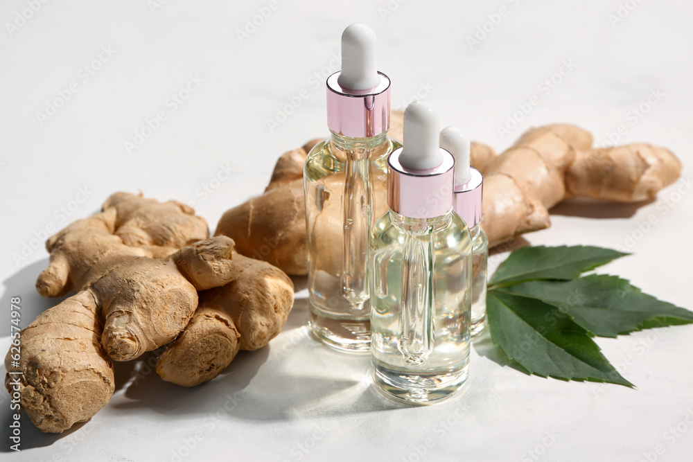 Bottles of ginger cosmetic oil and leaves on white background