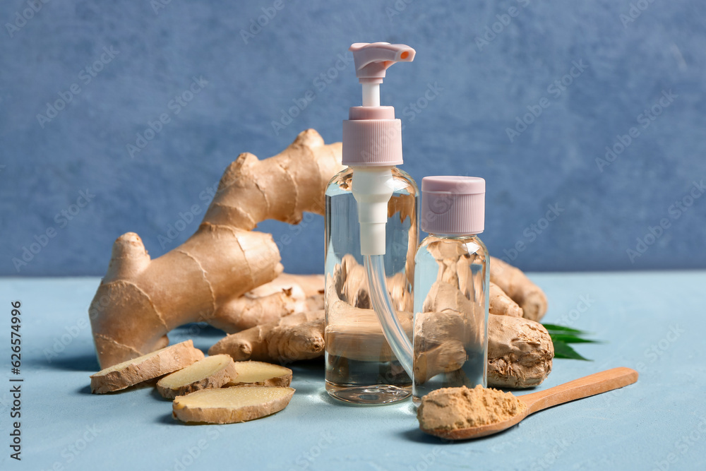 Bottles of ginger cosmetic oil and wooden spoon with dried powder on blue background