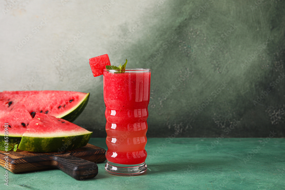 Glass of tasty watermelon juice with mint on green table