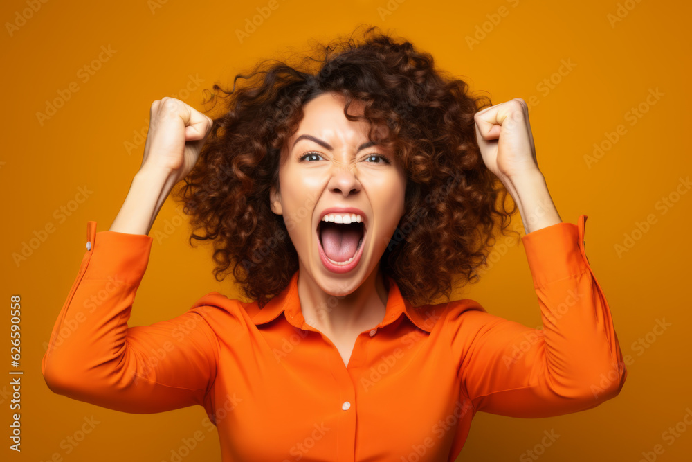 Woman in orange shirt with her hands on her head and fist in the air.