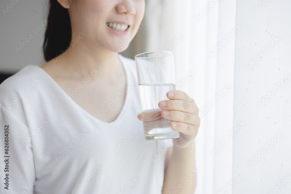 Healthy beautiful Asian young woman drinking pure water from glass at home. Caucasian female model h