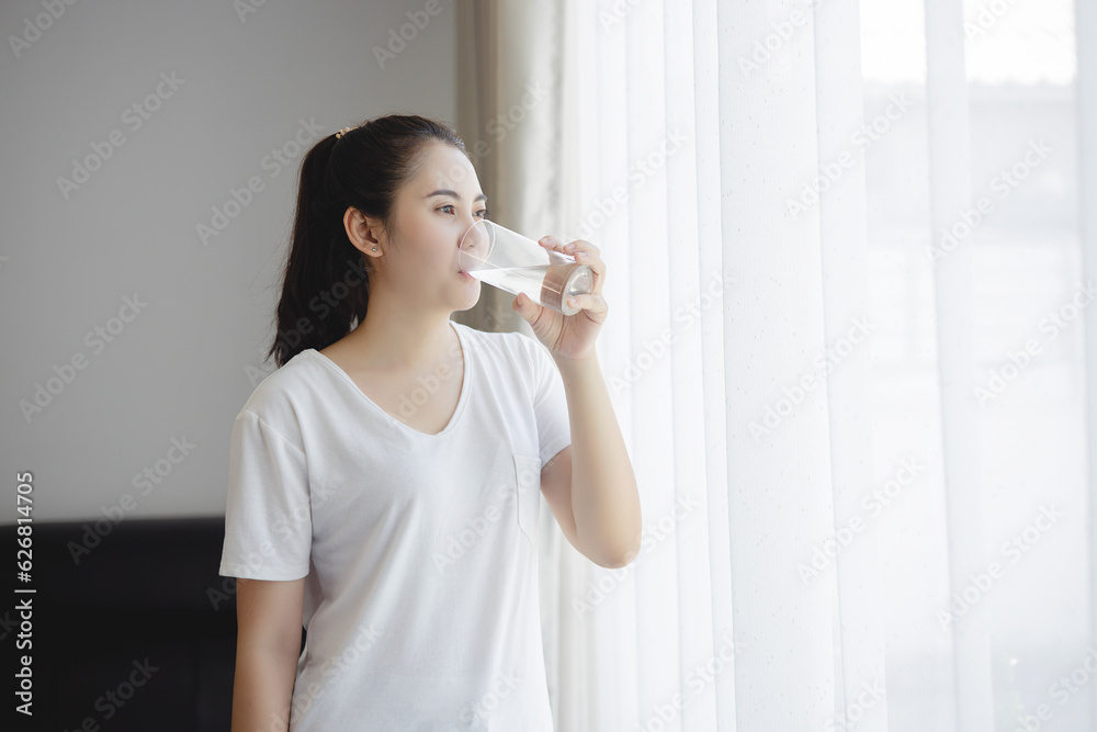 Healthy beautiful Asian young woman drinking pure water from glass at home. Caucasian female model h