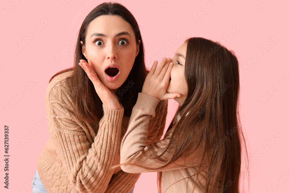 Little girl telling secret to her shocked mother on pink background