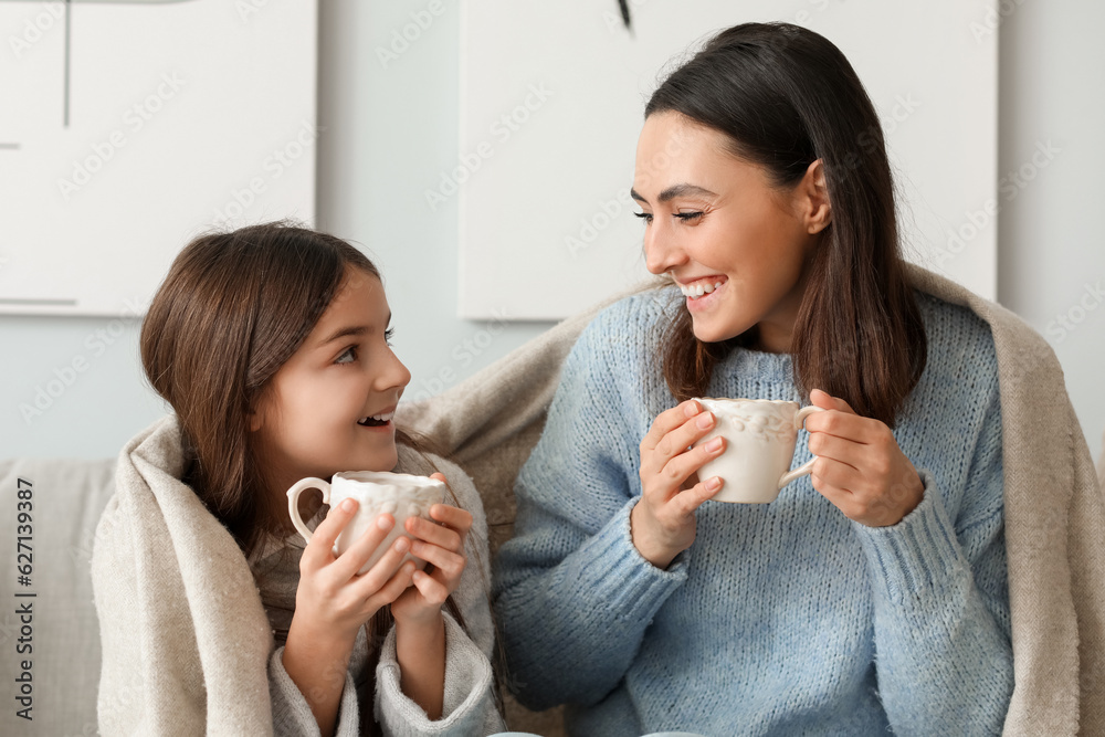 Little girl and her mother with cups of tea sitting at home