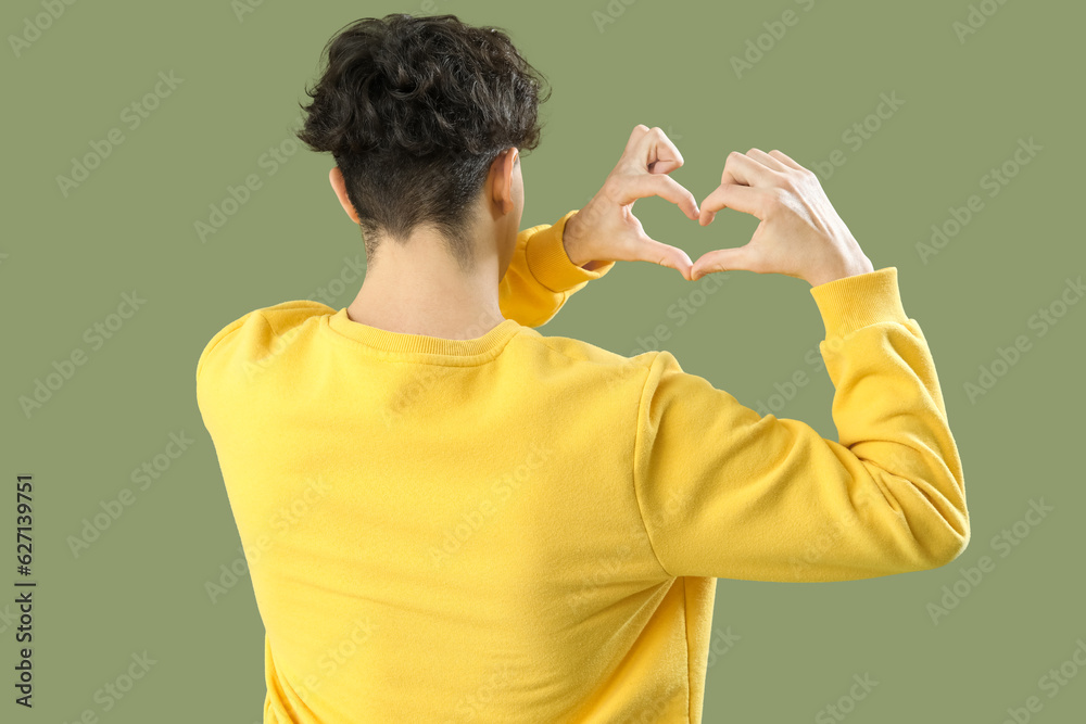 Handsome young man making heart with his hands on green background, back view