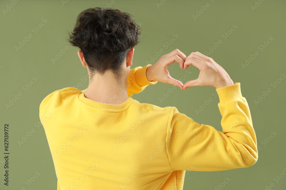 Handsome young man making heart with his hands on green background, back view