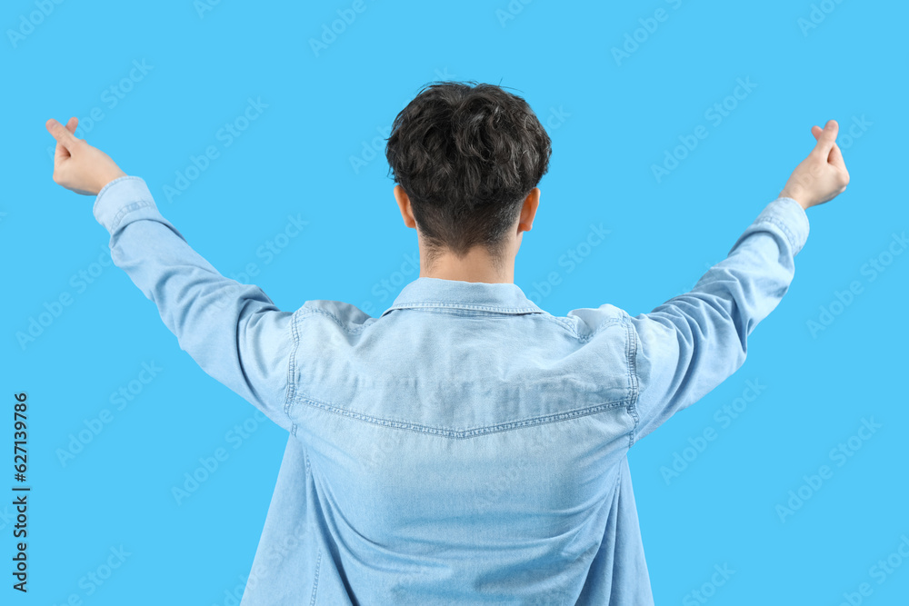 Handsome young man making heart with his fingers on light blue background, back view